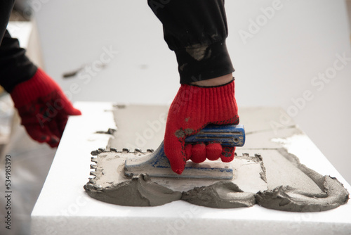 thermal insulation house. Close-up of worker hand, in red gloves with trowel applying glue on white rigid polyurethane foam she et for house
