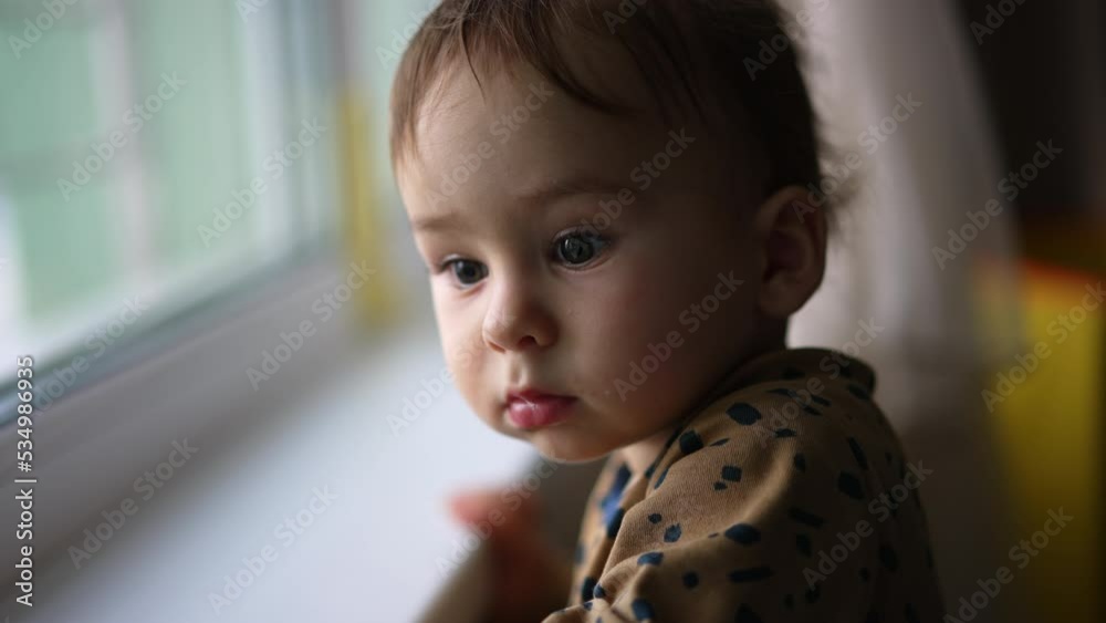 Adorable toddler boy standing at the windowsill. Baby looking curiously at window. Close up. Blurred backdrop. Adorable toddler boy standing at the windowsill. Baby looking curiously at window. Close up. Blurred backdrop.