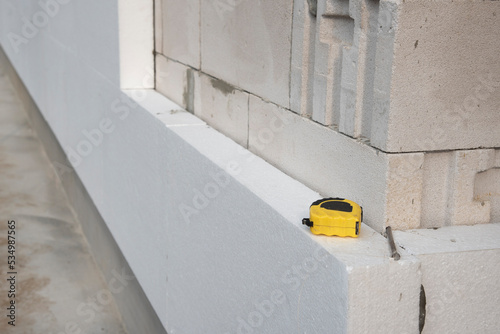 thermal insulation house. Black yellow tape measure on white rigid polyurethane foam sheet on wall.  photo