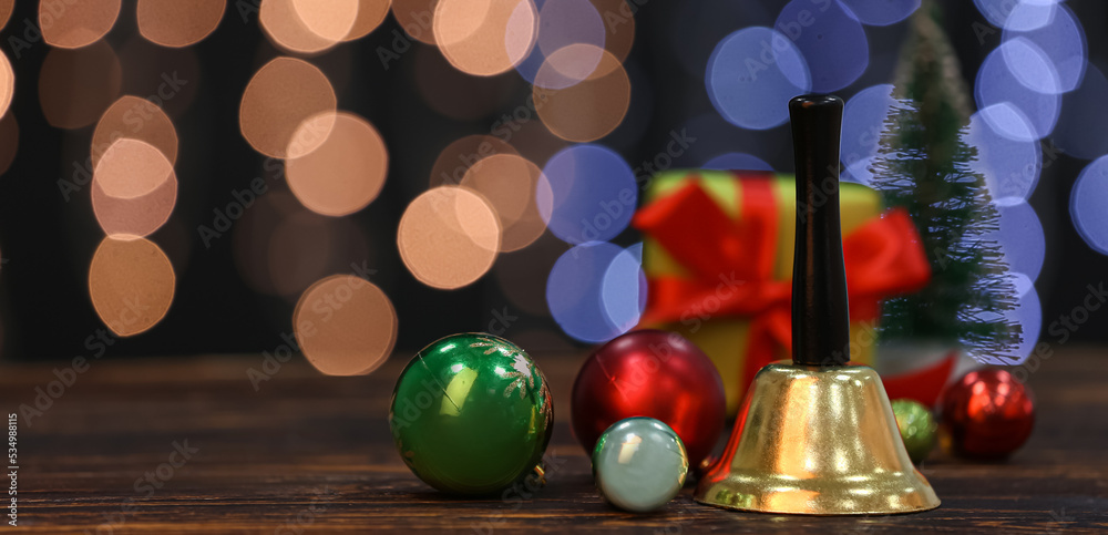 Golden Christmas bell and decorations on wooden table against blurred lights