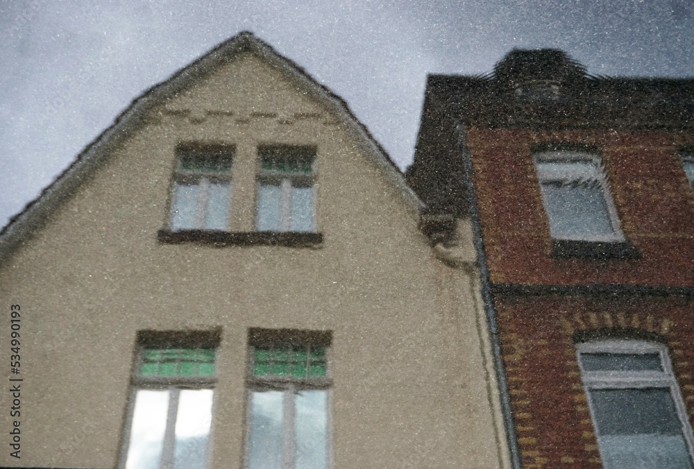 Regenwasserspiegelung mit zwei alten Häusern vor diesigem Himmel am Morgen im Herbst