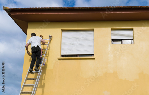 Rear view of a man on a ladder painting a house yellow, Spain