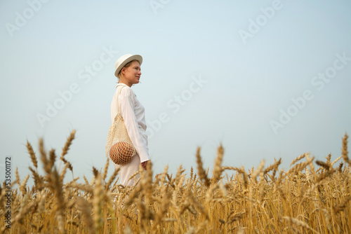 Woman in white clothes holds linen bag with freshly baked bread on wheat field background. Eco-friendly lifestyle concept. © Kate Stock