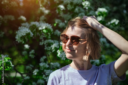 Attractive woman in sunglasses enjoying flowering of apple trees walking in spring garden. Happy female portrait.