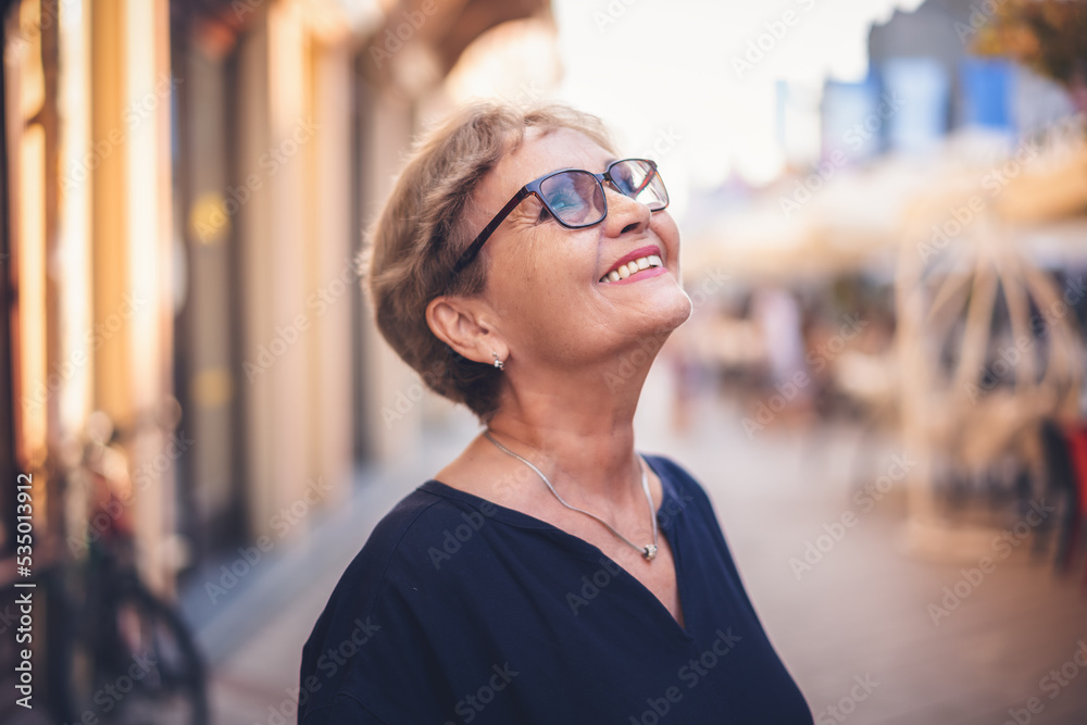 Portrait of happy active senior woman in glasses with a beautiful smile in profile walking in city on the street
