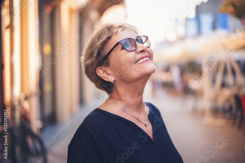 Obraz na płótnie Portrait of happy active senior woman in glasses with a beautiful smile in profile walking in city on the street w salonie