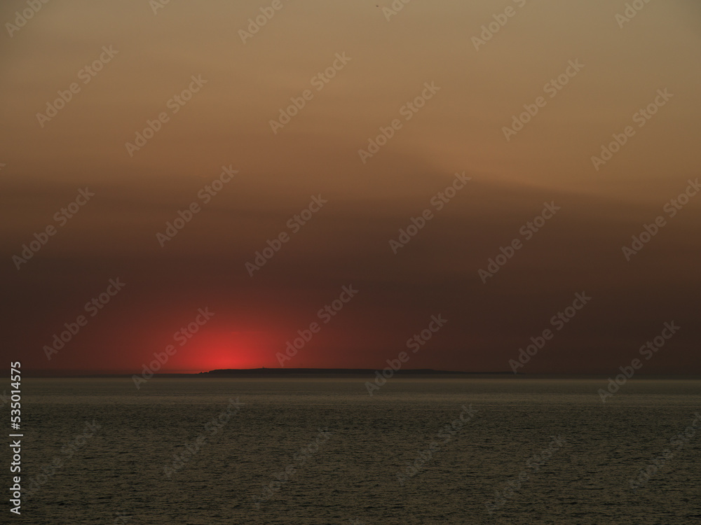 Fototapeta premium Red sunset over Lundy Island, viewed from Westward Ho. The sun has just dipped below the horizon.
