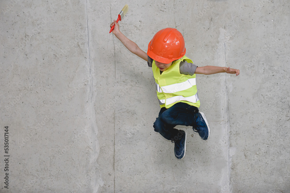 Boy wearing hardhat and safety vest jumping in front of concrete wall