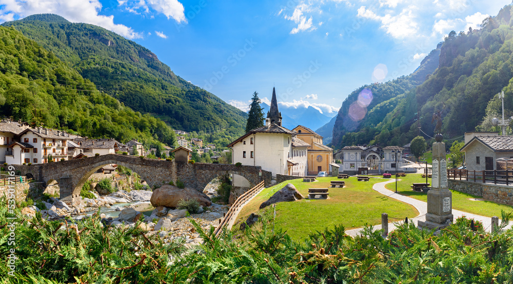 Lillianes, Aosta Valley. Italy. View of the stone bridge over the Lys stream, the Church of San Rocco and the cemetery. July 27, 2022.