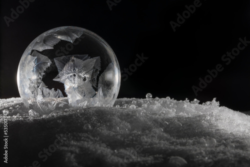 Close-up of frozen bubble black and white with small crystals on snow