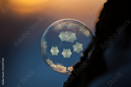 Close-up of frozen bubble against sky during sunset in orange blue light with small crystals