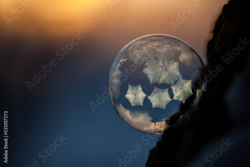Close-up of frozen bubble against sky during sunset in orange blue light with small crystals
