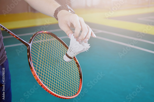 Badminton player holds racket and white cream shuttlecock in front of the net before serving it to another side of the court.