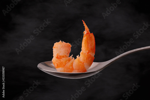 King prawn meat on a metal spoon on a dark background with steam.