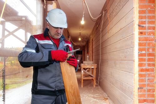 Builder at work. Man measures size of parquet. Concept of preparation for final finishing of walls or floors. Builder stands in unfinished building. Builder man with lumber. Parquet for renovation