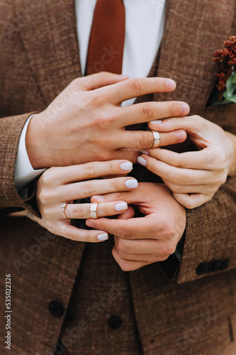 A stylish groom in a brown suit with a boutonniere and the bride put gold rings on their fingers at the ceremony. Wedding photography, close-up portrait.