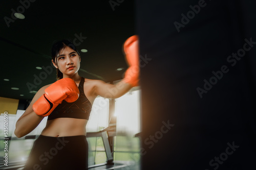 Asian young woman beginner training boxer punching with a punching bag in the gym.