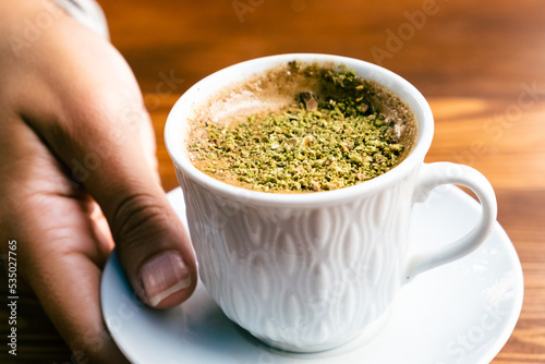 Pistachio coffee in a white cup. Woman with coffee in hand. Turkish coffee with pistachio.