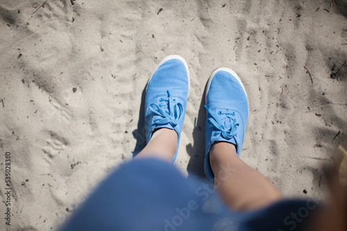 Women's feet in blue sneakers on white sand. white sand underfoot