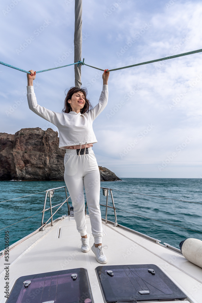Woman standing on the nose of the yacht at a sunny summer day, breeze developing hair, beautiful sea on background Woman standing on the nose of the yacht at a sunny summer day, breeze developing hair, beautiful sea on background