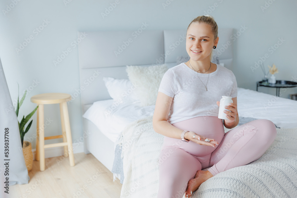 Happy young pregnant woman drinks vitamins pills in morning for baby health on bed. Concept conservation, examination healthy pregnancy Happy young pregnant woman drinks vitamins pills in morning for baby health on bed. Concept conservation, examination healthy pregnancy