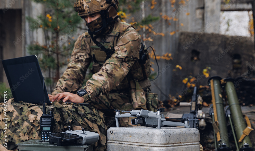 Obraz premium Mobile military base, soldier engineer transmits aerial pictures and data from drone to artillery. Concept of smart war by robots