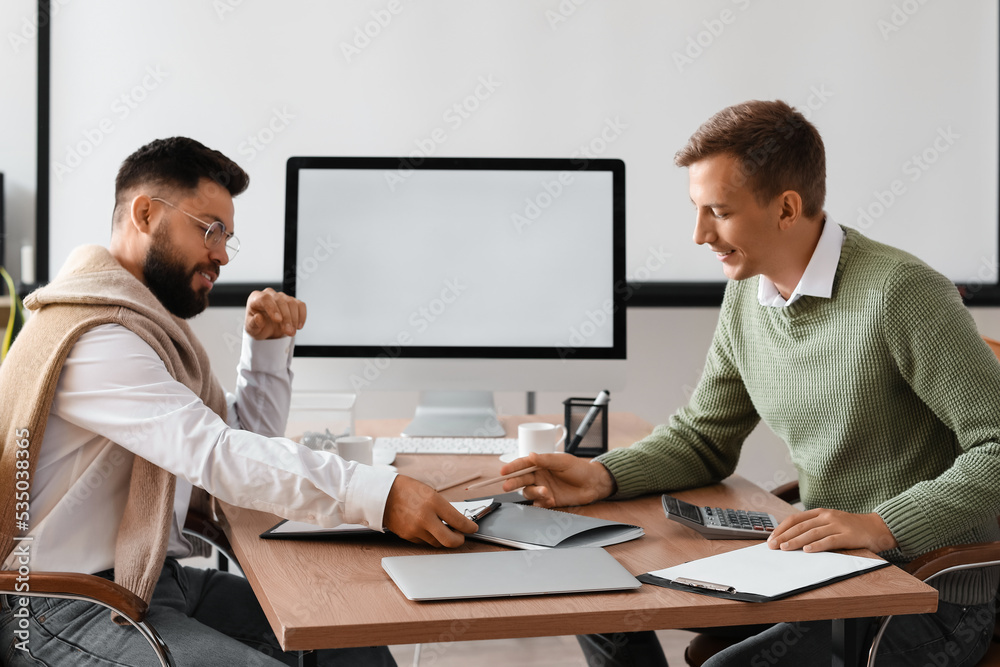 Male bank manager working with his colleague at table in office Male bank manager working with his colleague at table in office