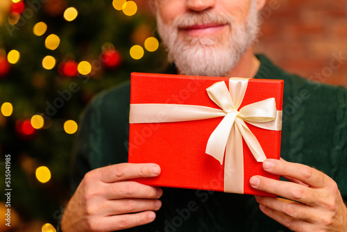 an elderly man in a green knitted with gift box near the Christmas tree