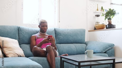 African Black transsexual man in stylish feminine clothes texting on cellphone on couch photo