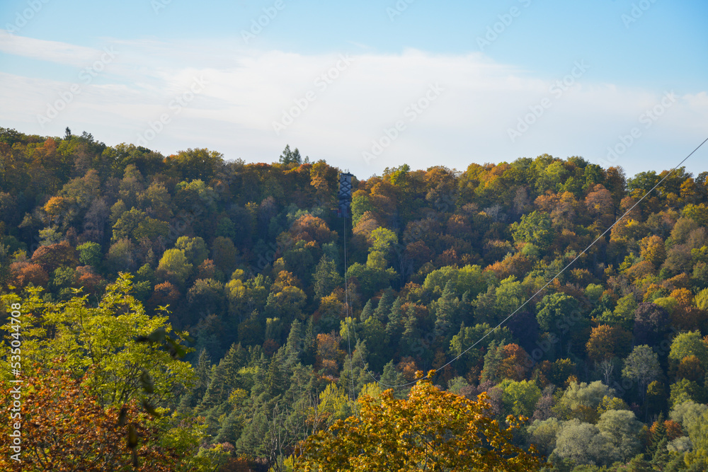Autumn landscape with colorful trees in the forest, over which metal cables for an aerial tram are stretched.