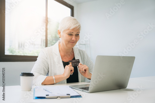 Woman holding a credit card and using a laptop computer to work online, shop online, and do banking online.