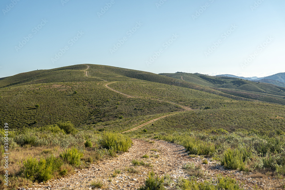 Landscape of gently rolling hills with winding road, against blue sky, on sunny day