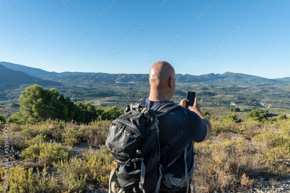 Rear view, male hiker using the phone to guide himself along the mountain path