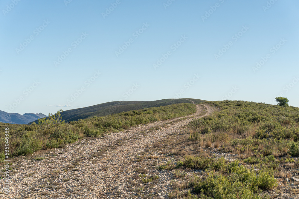 Landscape of gently rolling hills with winding road, against blue sky, on sunny day Landscape of gently rolling hills with winding road, against blue sky, on sunny day