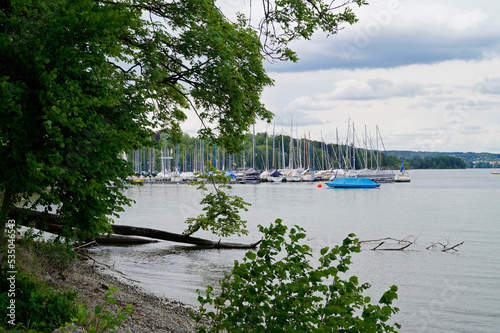 scenic view with sailing boats resting on  Lake Starnberg or Starnberger See surrounded with green trees in Bernried on a sunny day in May, Bavaria, Germany photo