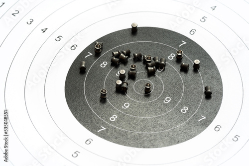 Circle shooting target and lots of metal pellets laying on top, object closeup, detail, nobody. Airgun sports, accessories. Pellet ammo, air guns ammunition, range aim training concept, no people photo