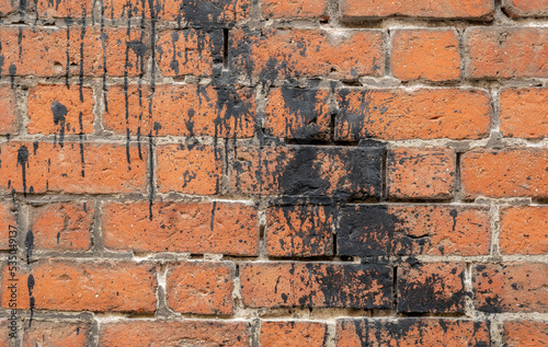 Simple old weathered brick wall splashed with black paint  tar  backdrop  background texture  wallpaper  nobody. Building side worn bricks black paint splash wall front view  closeup  no people