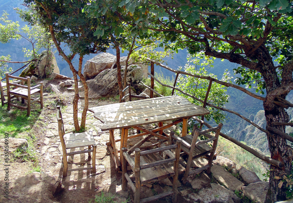 Armenian picnic in the mountains with a wooden table and chairs on top of a mountain near the edge of a picturesque gorge. Tatev, Armenia