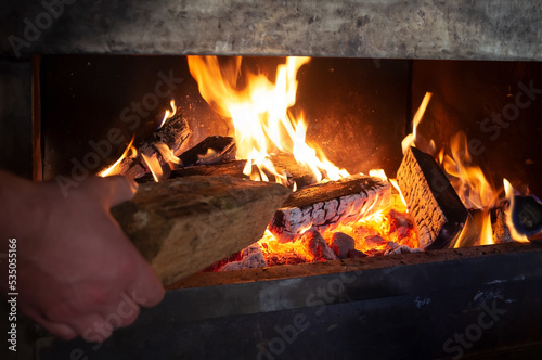 Hand puts a log on a fire to heat a home