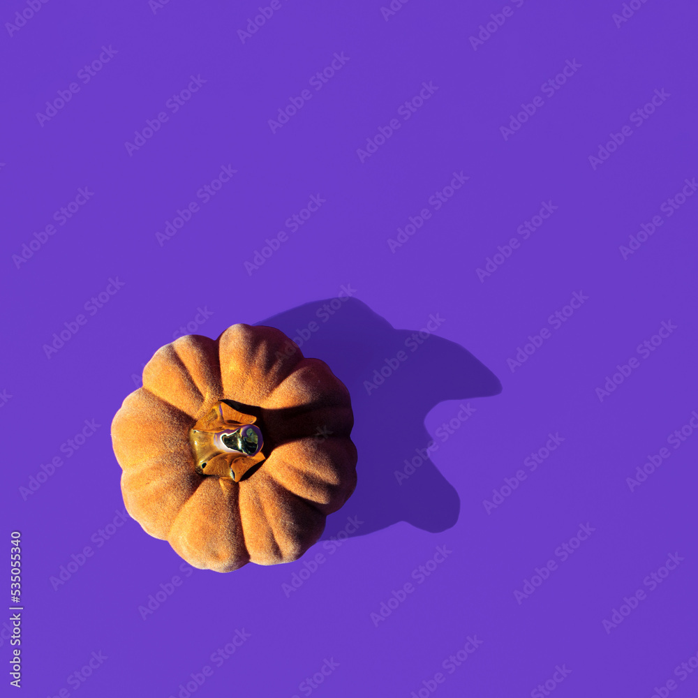 Decorative pumpkin and silhouette in the shape of a witch's face, minimal creative Halloween inspired layout on a purple background. 