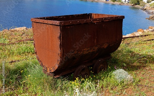 Old rusty coal tub or trolley on tracks, on the sea cliff in Megalo Livadi village, Serifos island, Greece