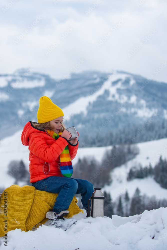 Kid boy hold mug cup with warm tea sit on sleigh ride ouside. Cold winter weather. Warm cup of hot drinks. Cute child holds a cup with a warm drink in the cold season. Winter clothes on the child.