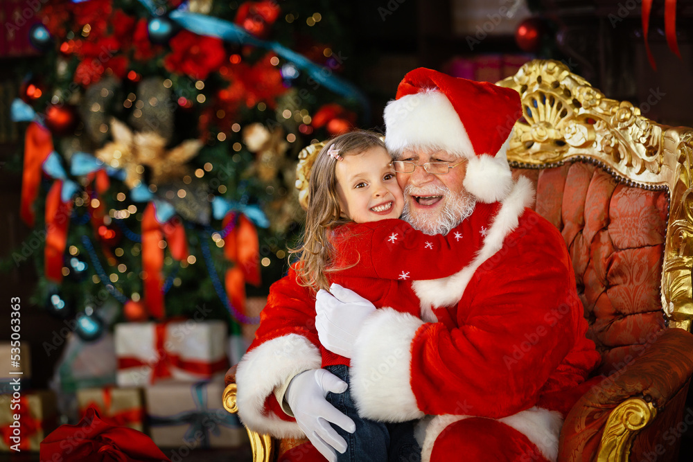 Santa Claus hugs the child and promises to fulfill his cherished wish. A smiling little girl on Santa's lap. Santa Claus hugs the child and promises to fulfill his cherished wish. A smiling little girl on Santa's lap.