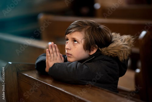 a little boy in a jacket prays in a dark catholic church at a children's mass