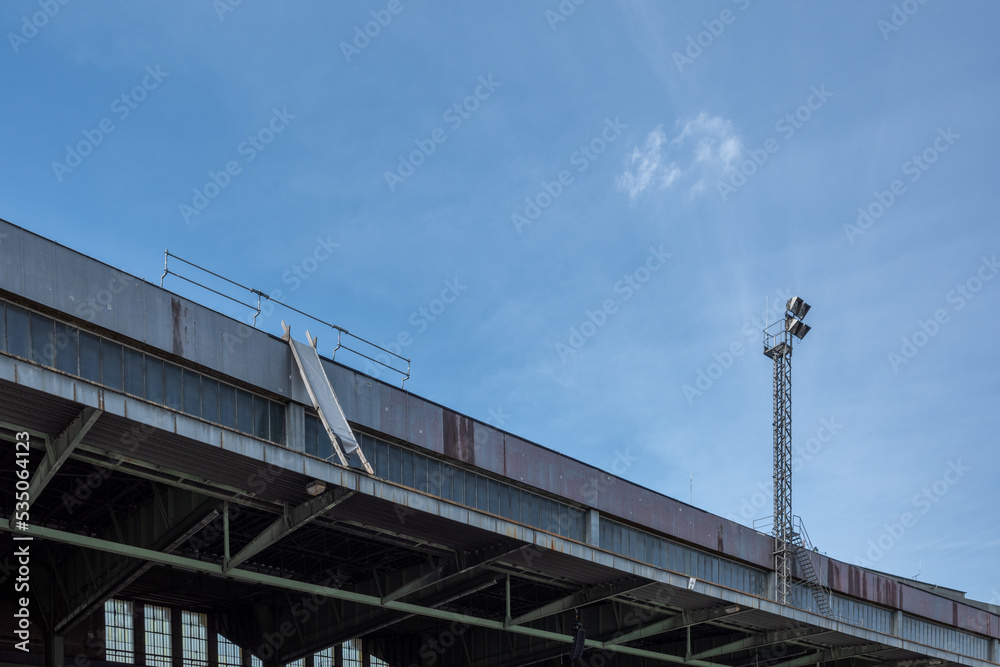 Outdoor sunny view of the roof with cantilever structure and lamp tower at former airport terminal in Berlin, Germany. Outdoor sunny view of the roof with cantilever structure and lamp tower at former airport terminal in Berlin, Germany.