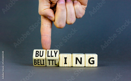 Bullying and belittling symbol. Concept words Bullying and Belittling on wooden cubes. Businessman hand. Beautiful grey table grey background. Business bullying and belittling concept. Copy space.