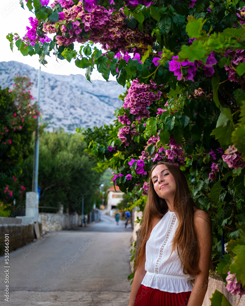 Fototapeta premium beautiful elegant woman in a white lace blouse and long red skirt walks through the Mediterranean town of orebić on the peljesac peninsula; holiday in croatia