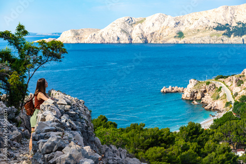 beautiful girl walks on the rocks on the shore of the adriatic enjoying the wonderful views in the background; vacation in croatia on krk island; hiking by vrzenica beach trail photo
