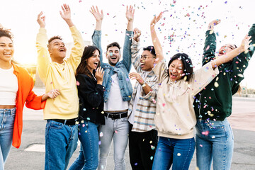 Group of diverse young friends celebrating together enjoying party throwing confetti outdoors - Happiness and celebration concept with millennial multiracial friends laughing and having fun