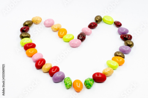 Heart made of colorful candy dragees. Dragee candies isolated on white background. Heart figure made of candy. 
